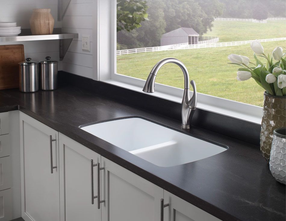 Modern kitchen sink with black countertop, white cabinets, and a window overlooking a green lawn