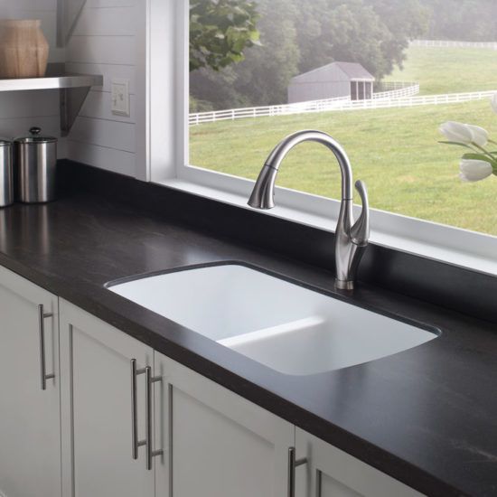 Modern kitchen sink with dark countertop and large window overlooking a green yard