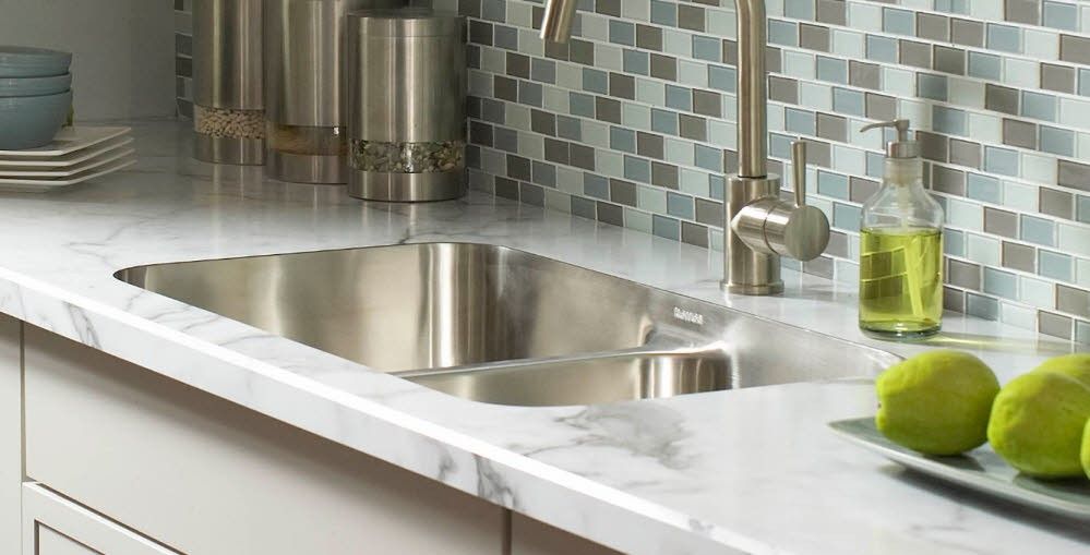 Modern kitchen countertop with stainless steel sink, marble surface, mosaic backsplash, and green apples