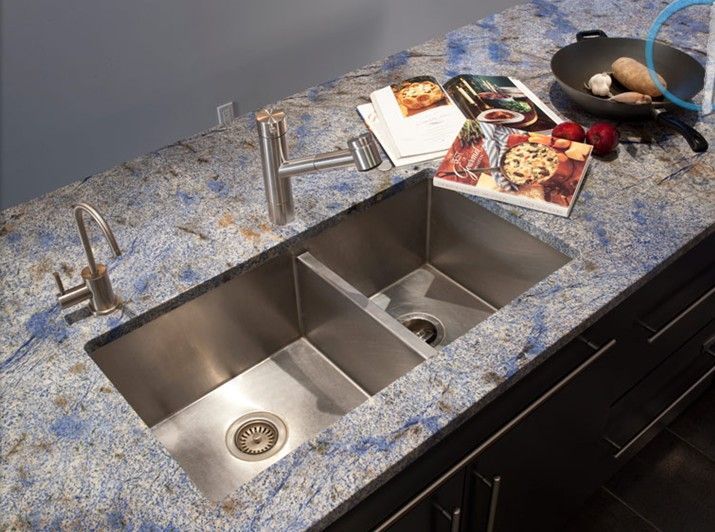 Modern kitchen sink with blue granite countertop, double basins, faucets, and cookbooks beside a frying pan