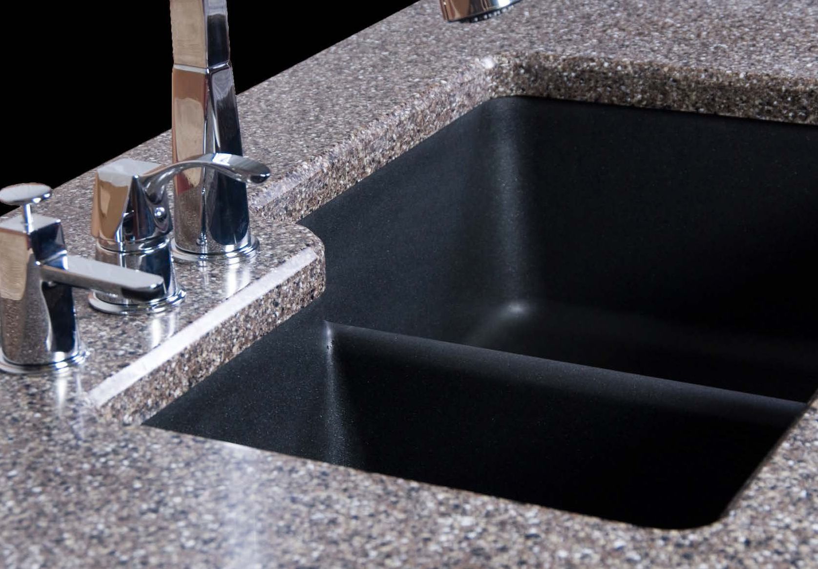 Stainless steel kitchen sink with chrome faucet and black basin inset in speckled countertop