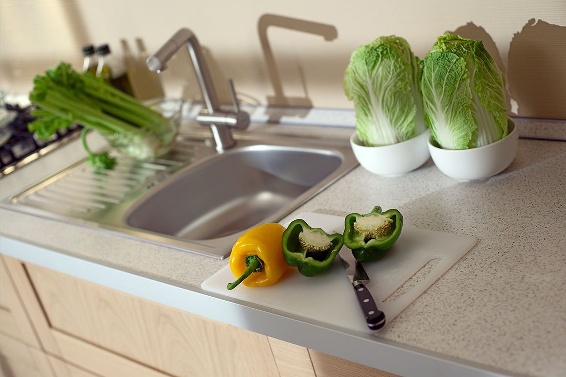 Kitchen countertop with bell peppers, leafy greens, and white bowls beside a sink