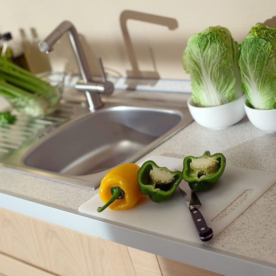 Kitchen counter with sink, yellow and green peppers, and a knife beside a white bowl of lettuce.