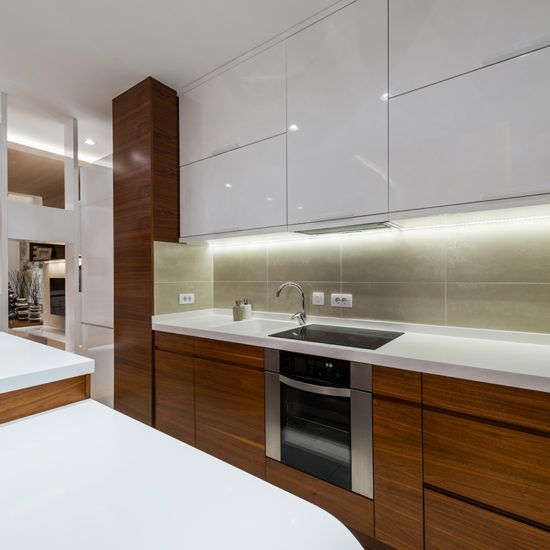 Modern kitchen with wood cabinets, white countertops, and stainless steel appliances under under-cabinet lighting