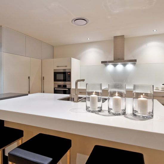 Modern white kitchen with island, bar stools, built-in oven, and lit range hood.