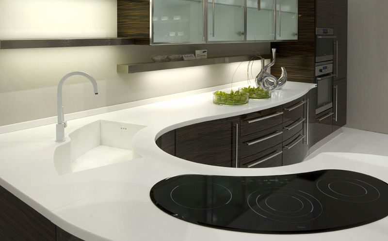 Modern white kitchen with curved black countertop, sink, cabinets, and stovetop on the island