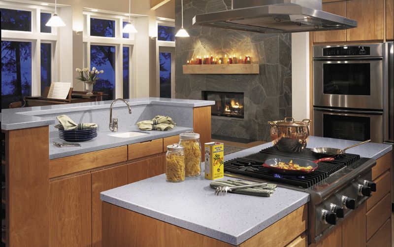 Modern kitchen with large windows, island cooktop, gray counters, wood cabinets, and stainless steel appliances