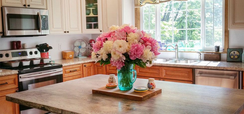 Bright kitchen with a large wooden island and a vase of pink flowers by the window
