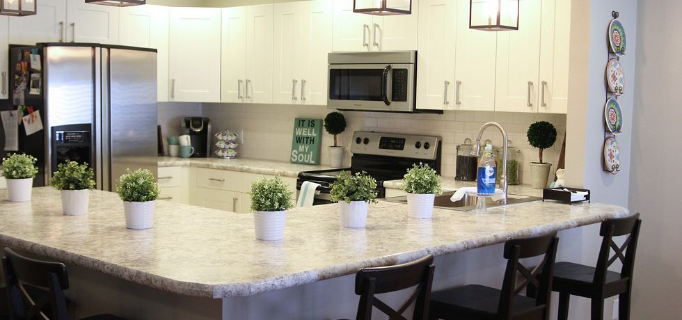 Modern kitchen with a large granite island, white cabinets, and bar stools.
