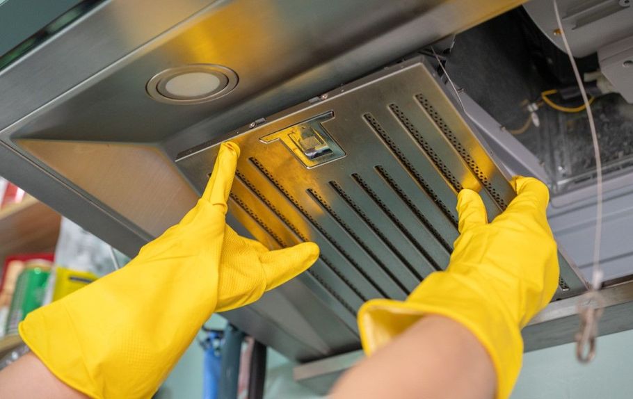 Hands in yellow gloves removing a metal range hood filter for cleaning in a kitchen