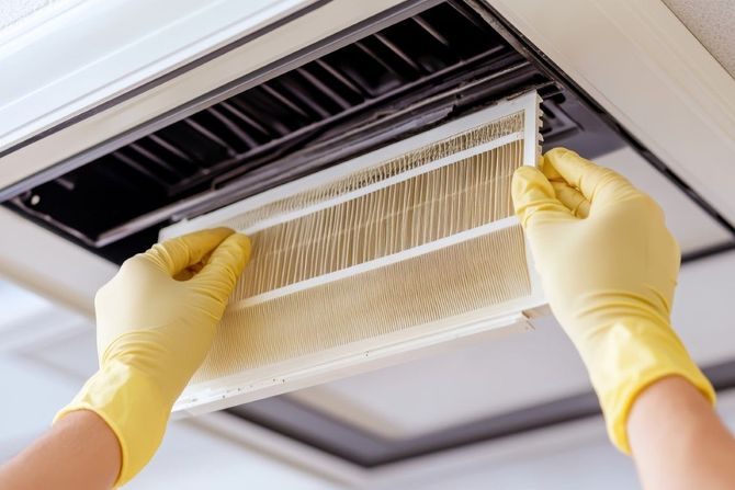 Gloved hands replacing a dirty HVAC air filter in a ceiling vent