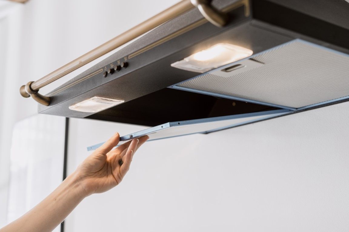 Hand opening a stainless steel range hood filter above a stovetop