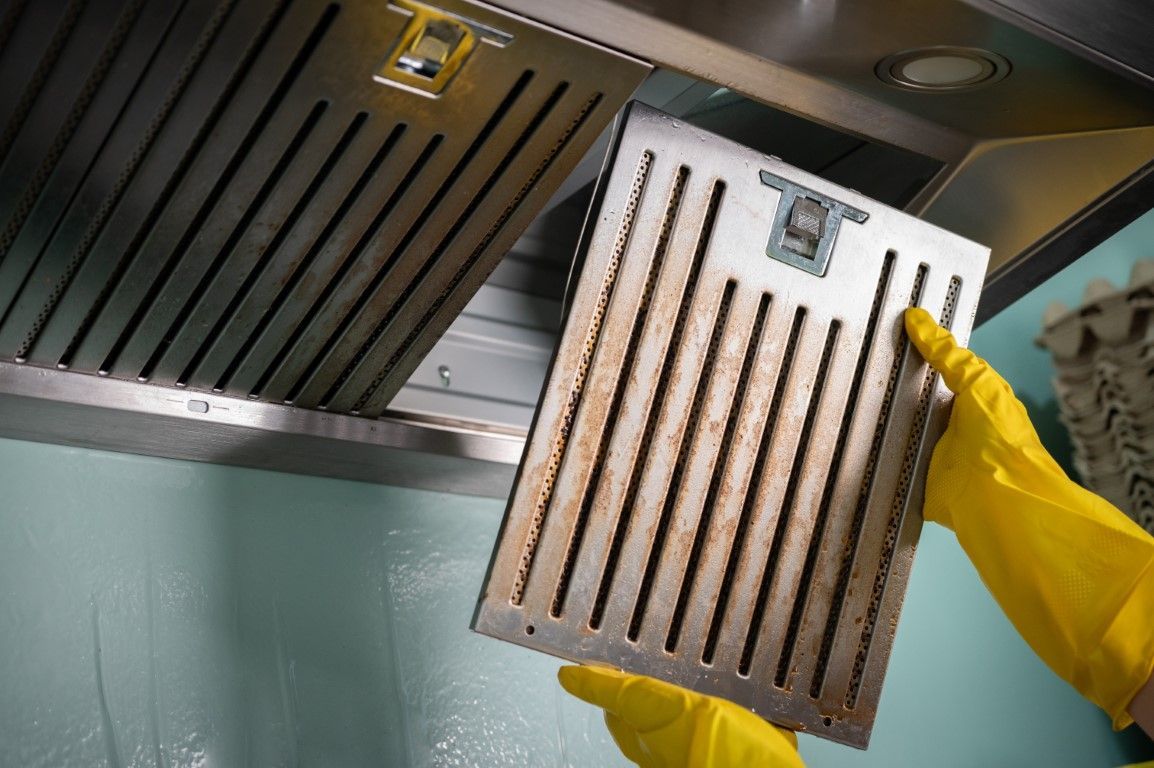 Gloved hands holding a metal grease filter under a kitchen range hood