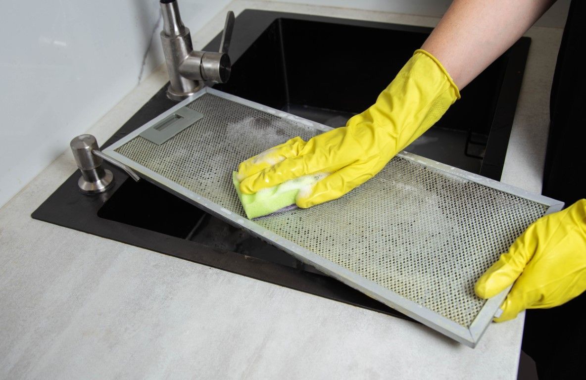 Gloved hands cleaning a metal mesh tray over a sink