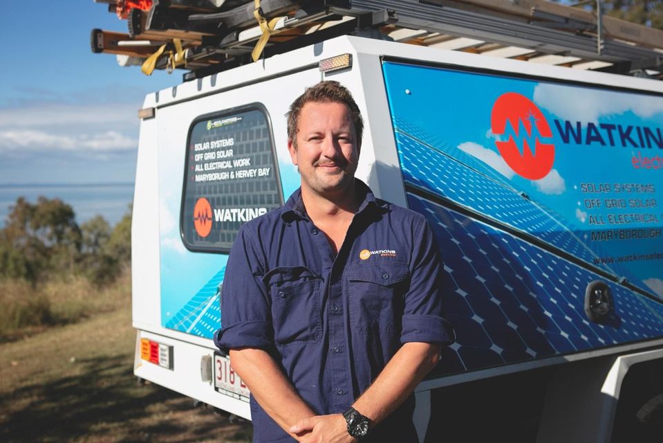 Man in work shirt stands by solar panel van, smiling — Watkins Electrical In Pialba, QLD
