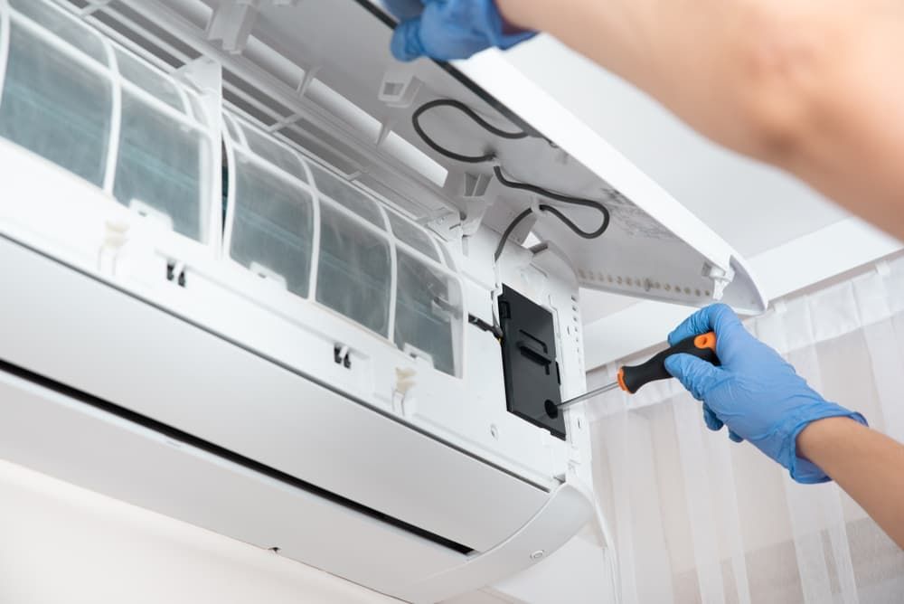 A Person is Fixing an Air Conditioner With a Screwdriver — Watkins Electrical In Pialba, QLD