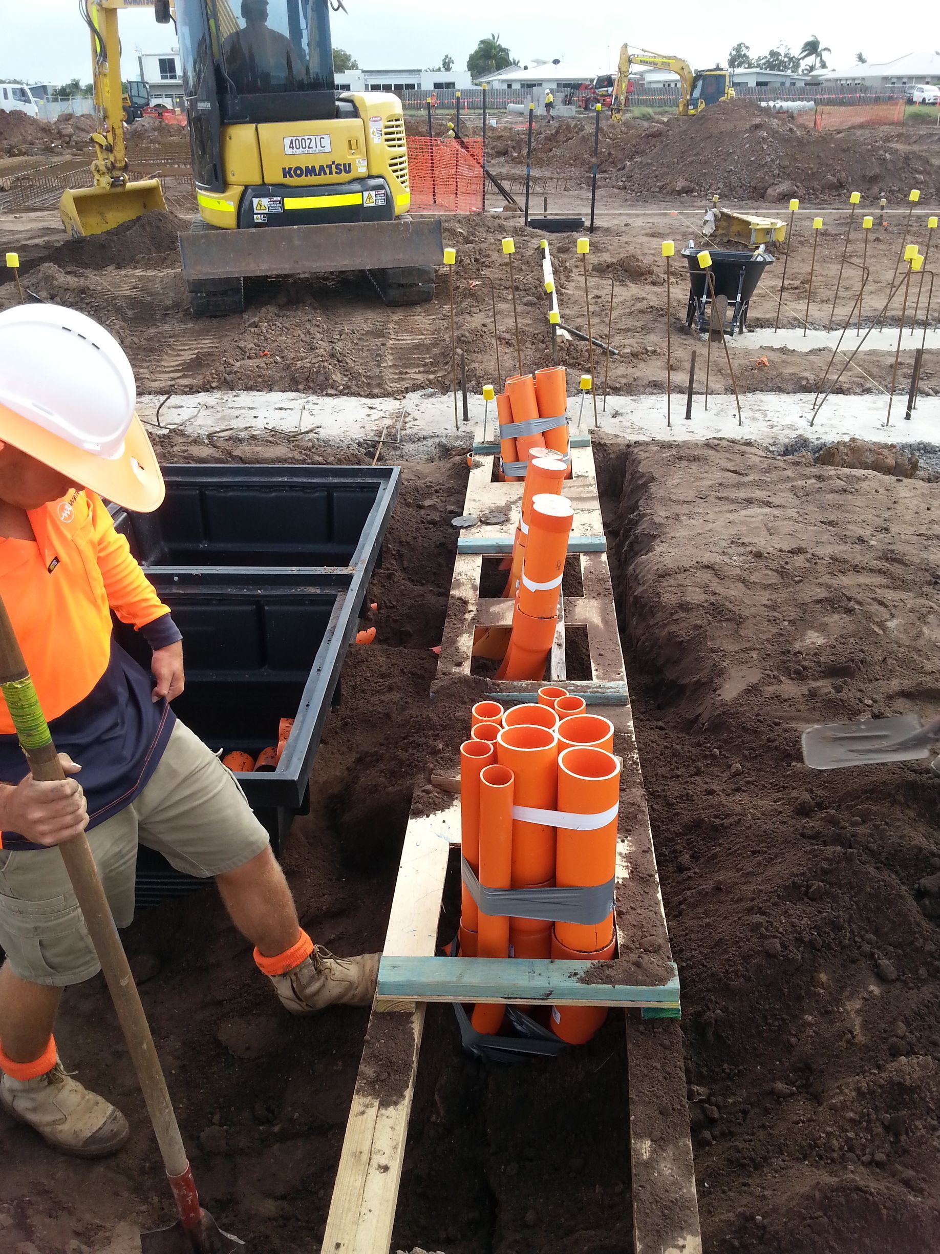Construction worker inspecting orange electrical conduit pipes in trench at building site — Watkins Electrical In Pialba, QLD