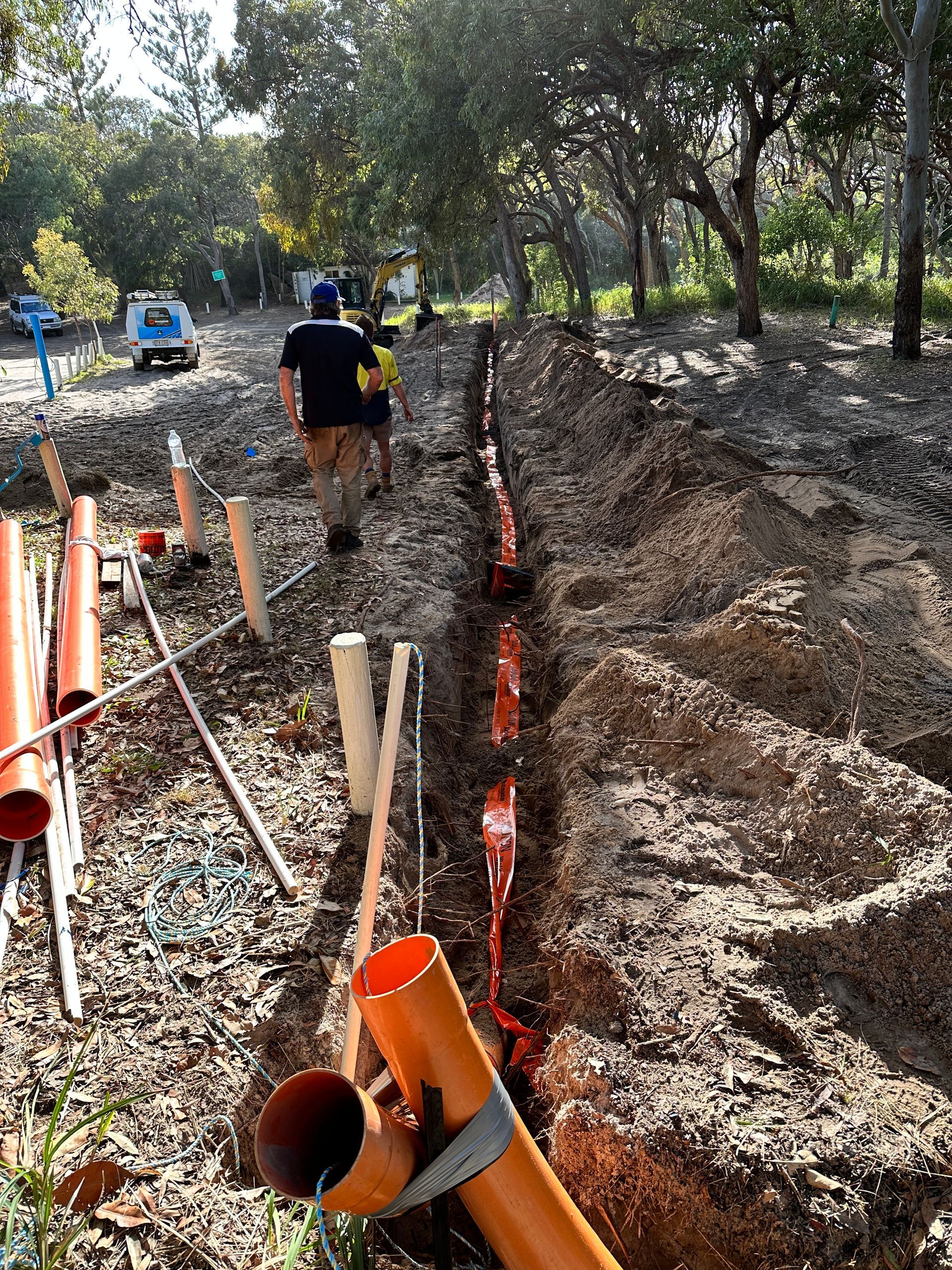 Construction site with an open trench, orange pipes, and workers in a wooded area — Watkins Electrical In Pialba, QLD