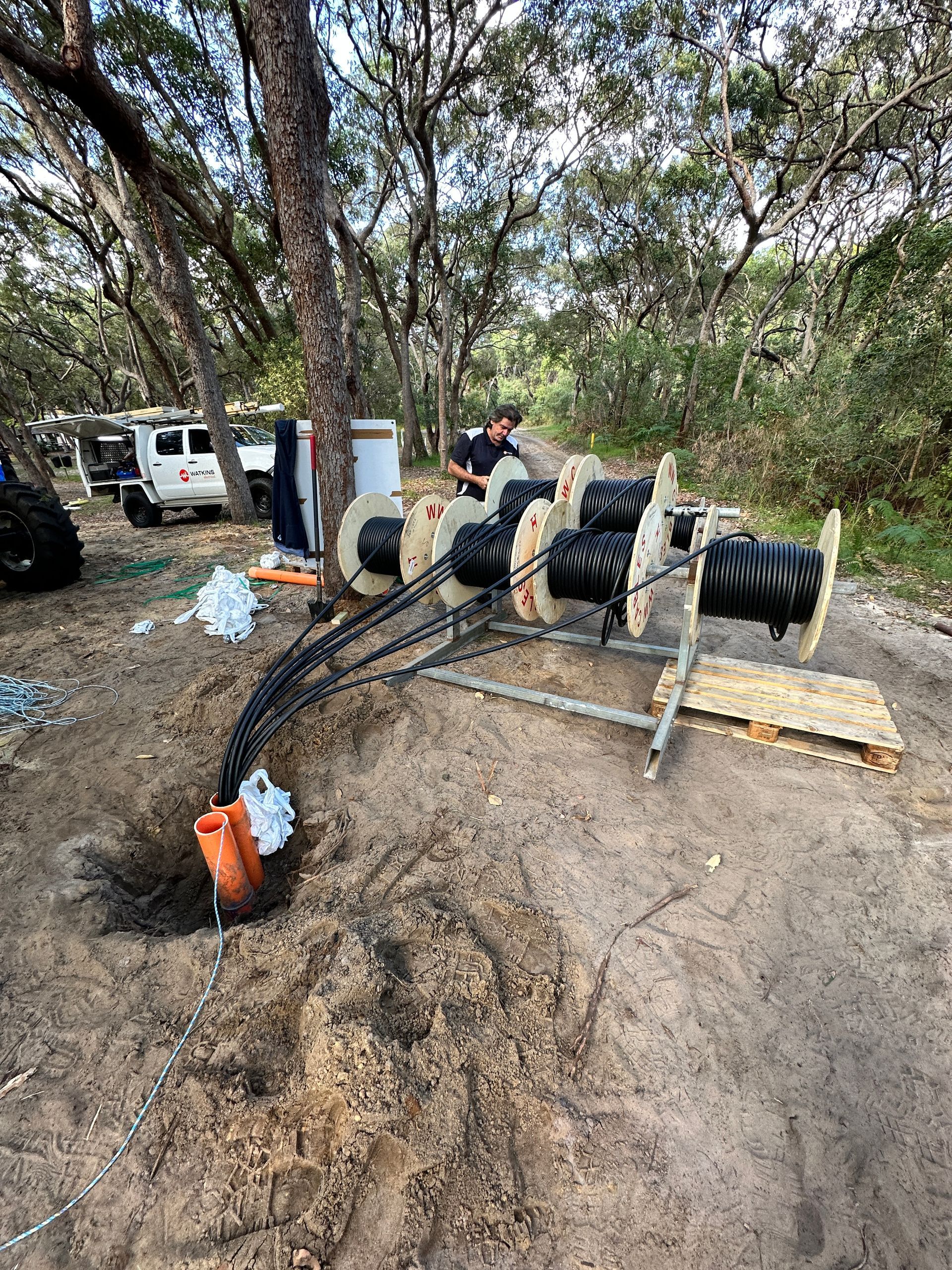 Man with cables on spools in a wooded area. Construction work in progress — Watkins Electrical In Pialba, QLD