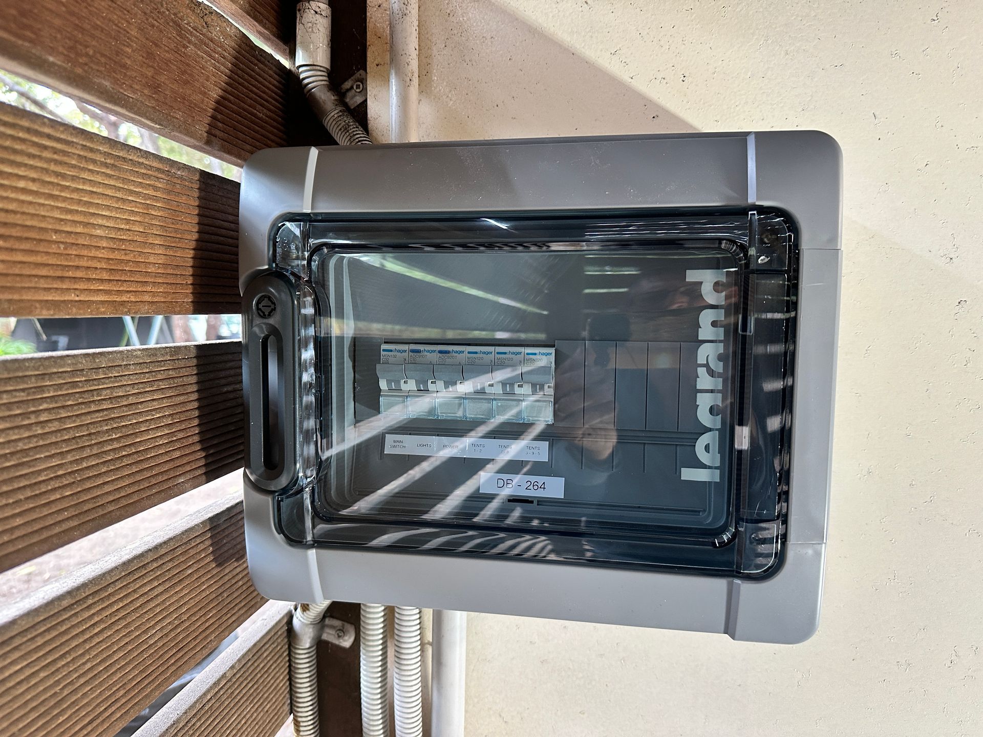 Outdoor Legrand electrical panel with a clear cover mounted on a wall near blinds — Watkins Electrical In Pialba, QLD