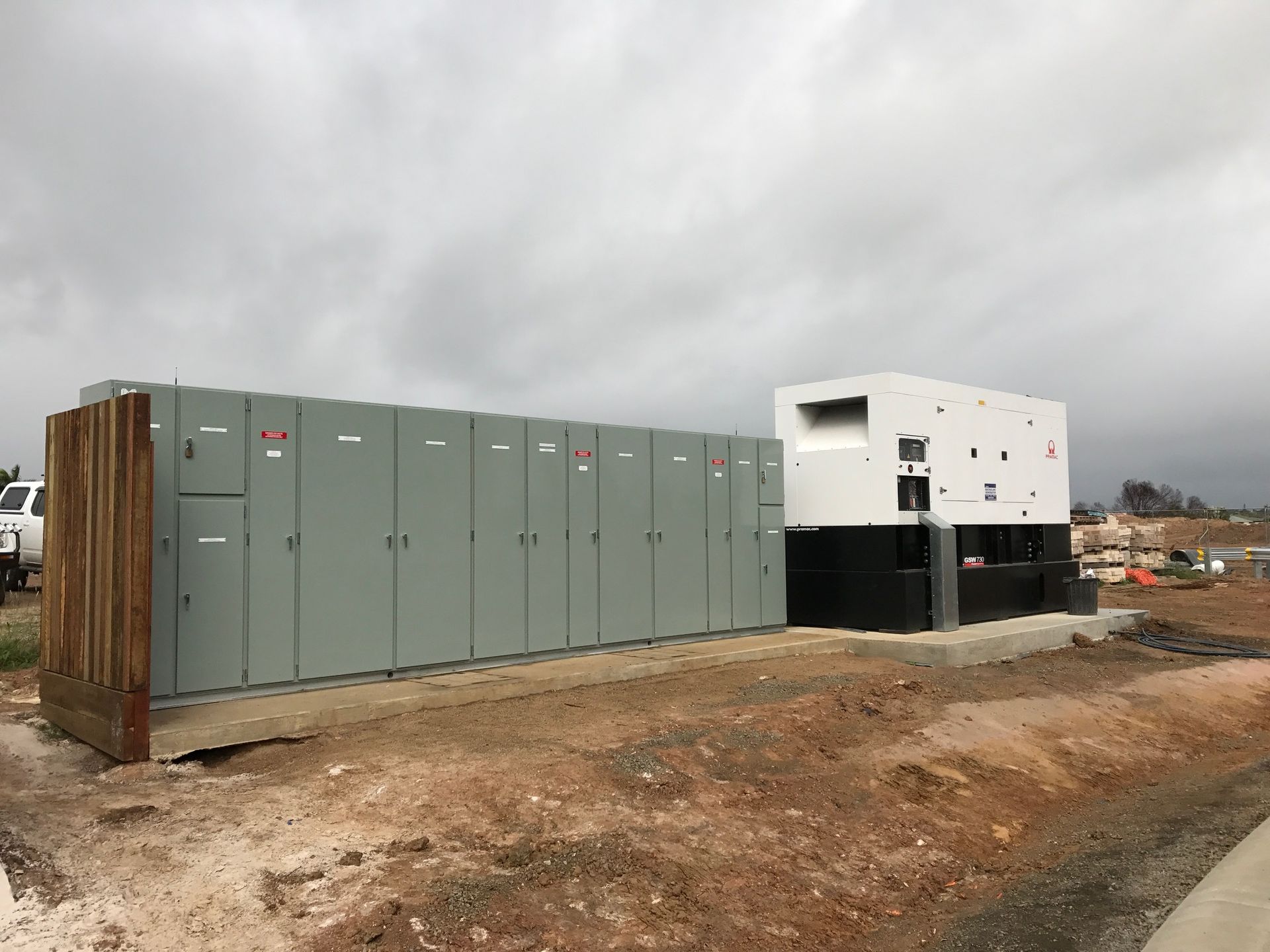 Gray electrical equipment and a white building on a dirt lot under a cloudy sky — Watkins Electrical In Pialba, QLD