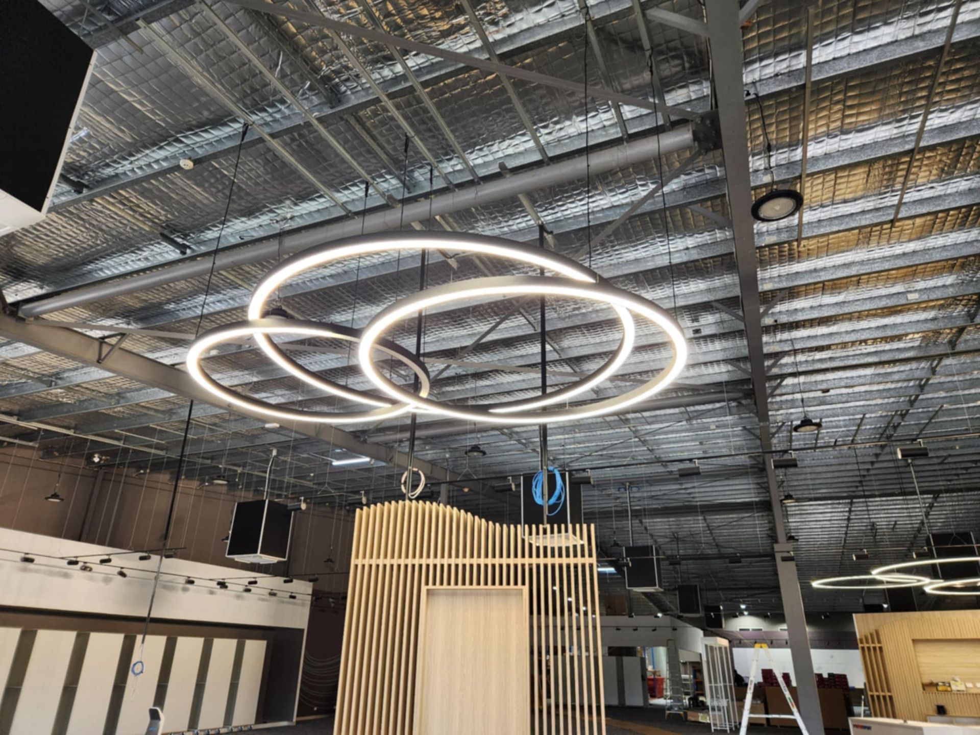 Modern circular LED light fixture hanging from a metal ceiling in a large room — Watkins Electrical In Pialba, QLD