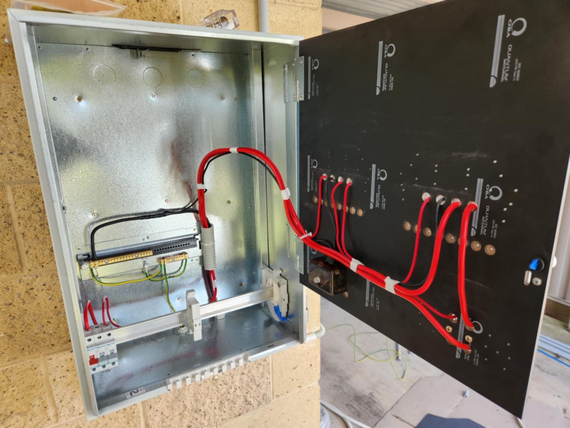 Open electrical panel, showing wiring, breakers, and components, mounted on a brick wall — Watkins Electrical In Pialba, QLD