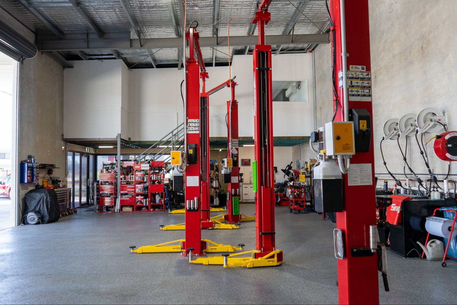 Red and yellow car lifts in a brightly lit auto repair shop — Watkins Electrical In Pialba, QLD