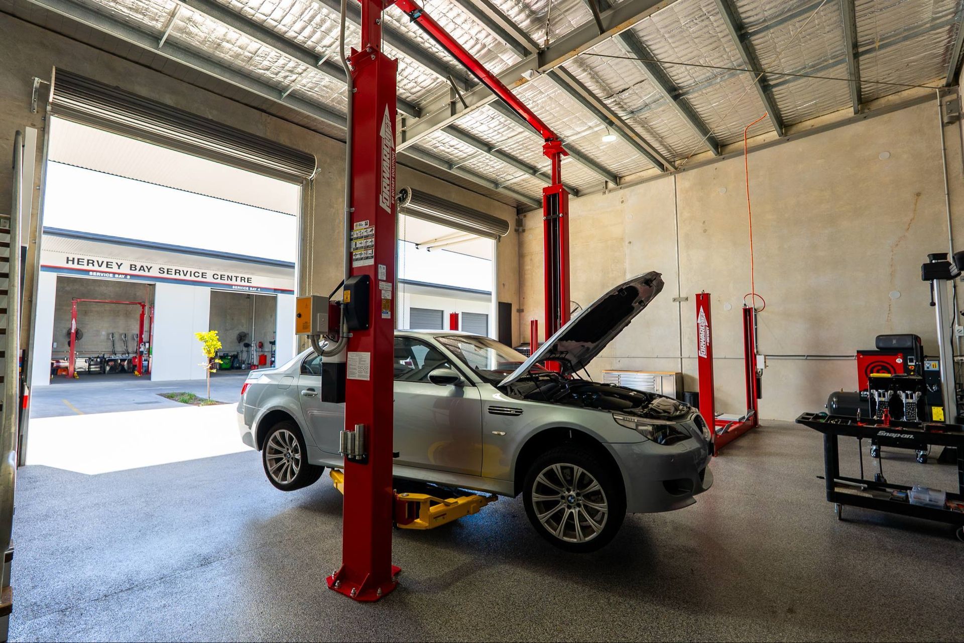 Silver car raised on a lift in a garage with open hood; red lift posts — Watkins Electrical In Pialba, QLD