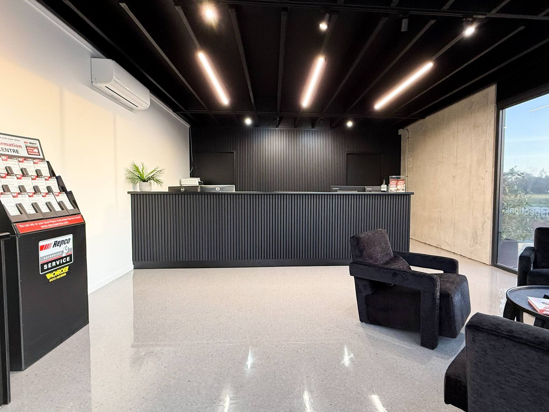 Reception area with black counter, seating, and product display.  Modern design with light and dark tones — Watkins Electrical In Pialba, QLD