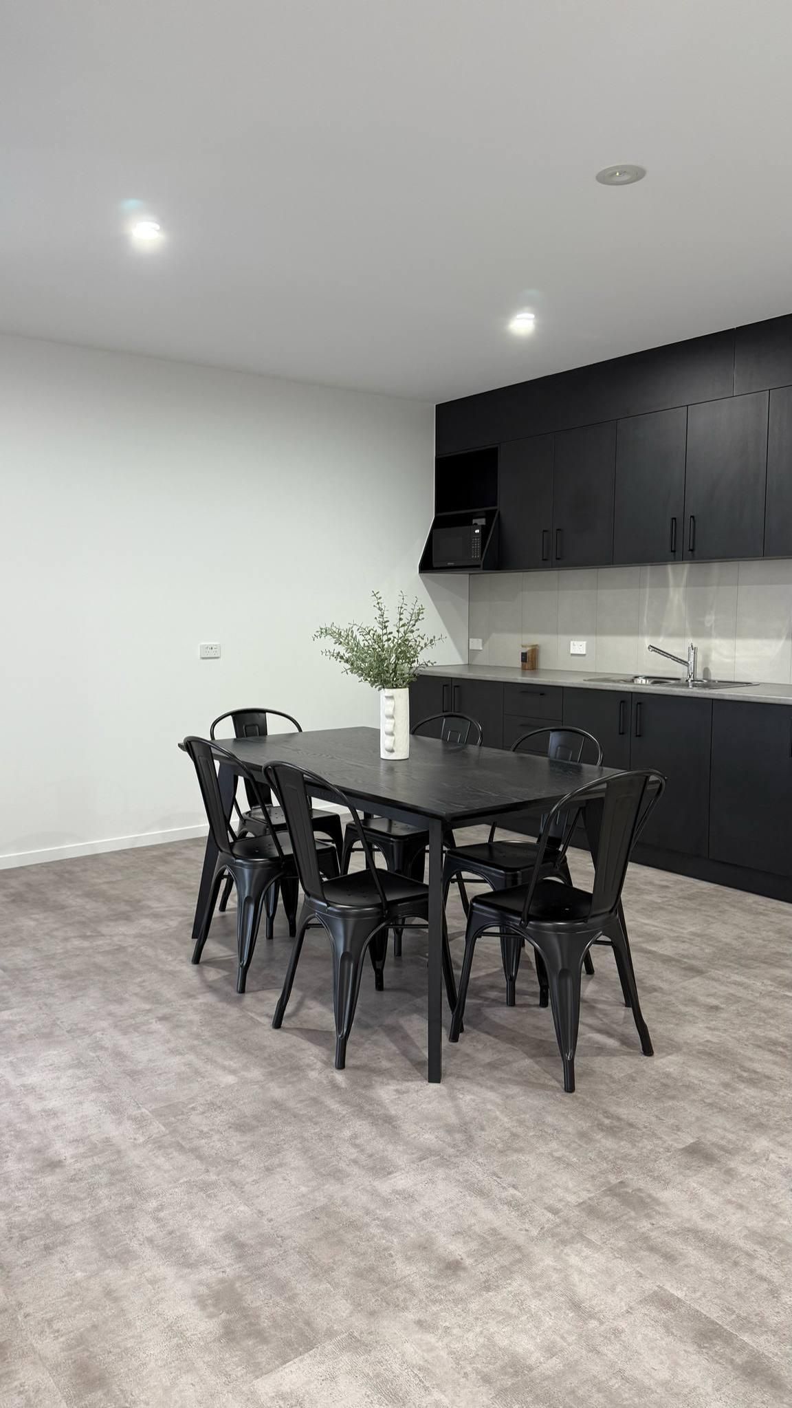 Black dining table and chairs in a modern kitchen with gray flooring and dark cabinets. — Watkins Electrical In Fraser Coast, QLD