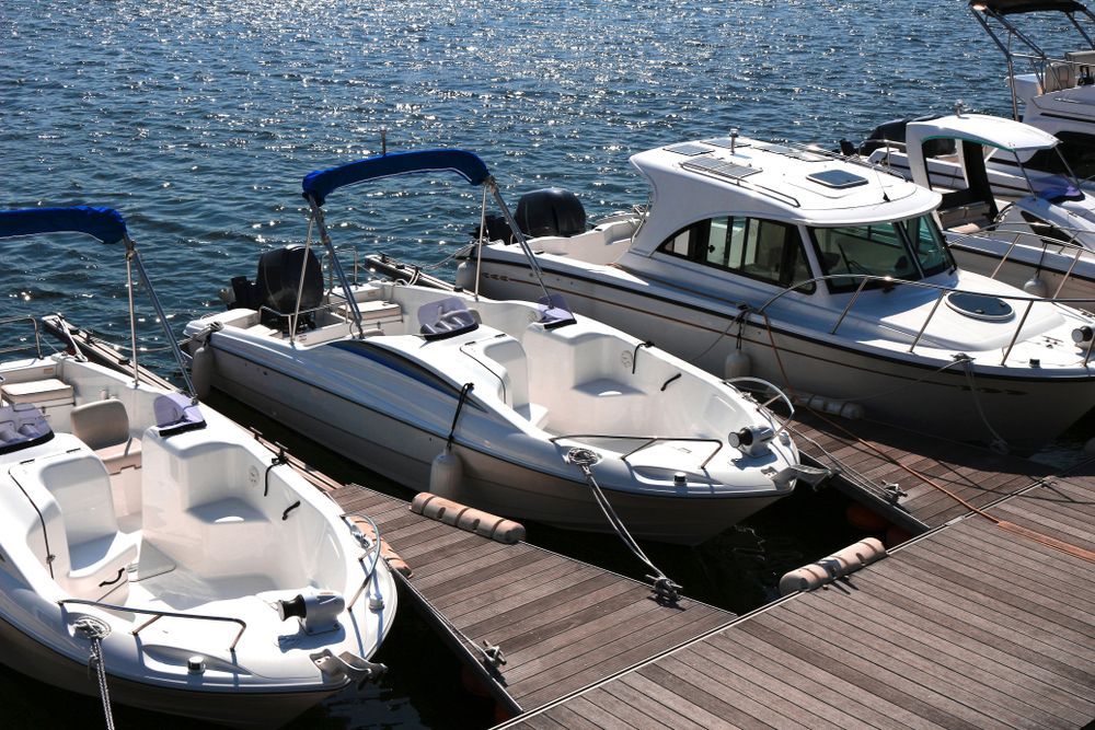 Three white motorboats docked on a wooden pier beside rippling blue water.