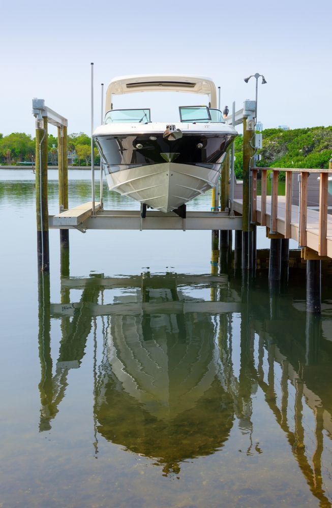 White yacht moored at a dock, reflected in calm water on a sunny day.