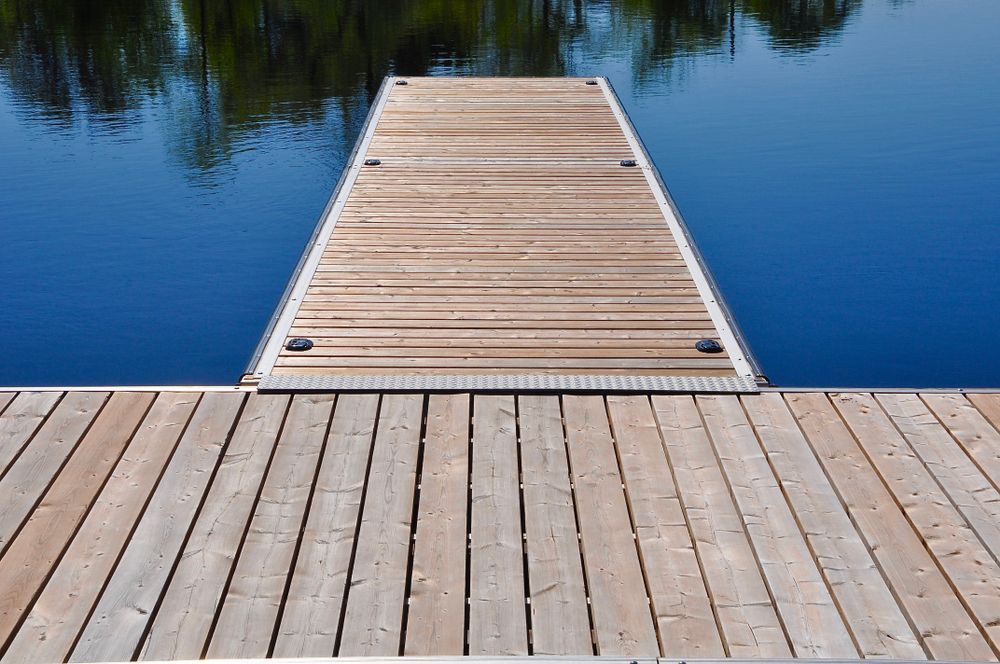 Wooden dock extending into calm blue water, with trees reflected on the surface.