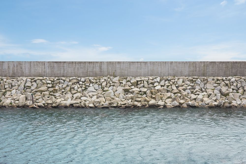 Rock breakwater wall beside calm blue water under a clear sky