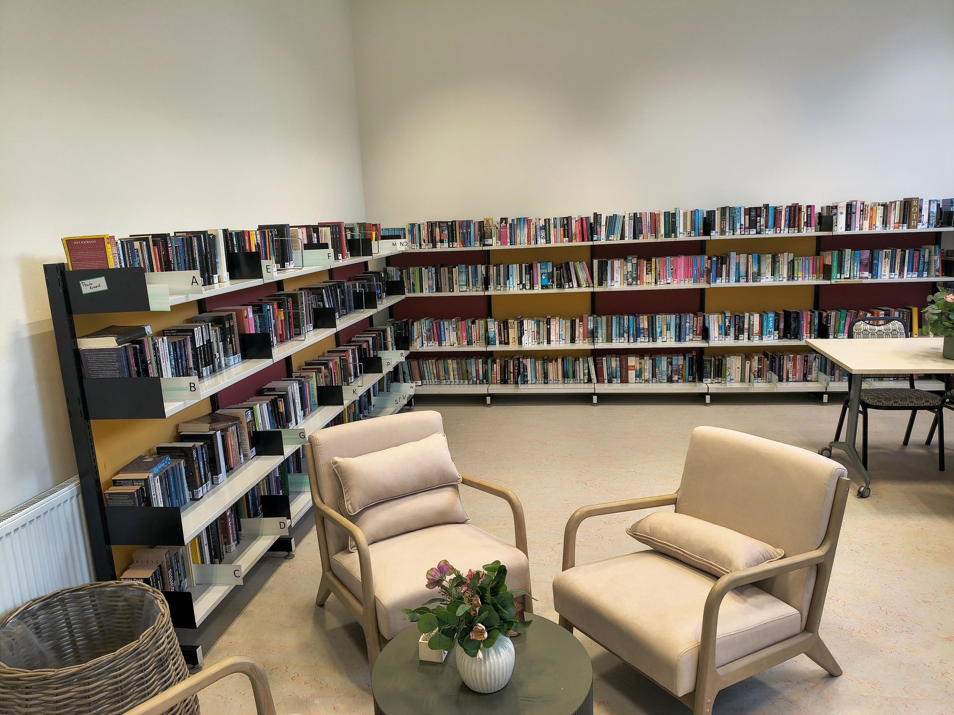 Een rustig leeshoekje met twee beige fauteuils, een tafeltje en boekenkasten langs de muren.