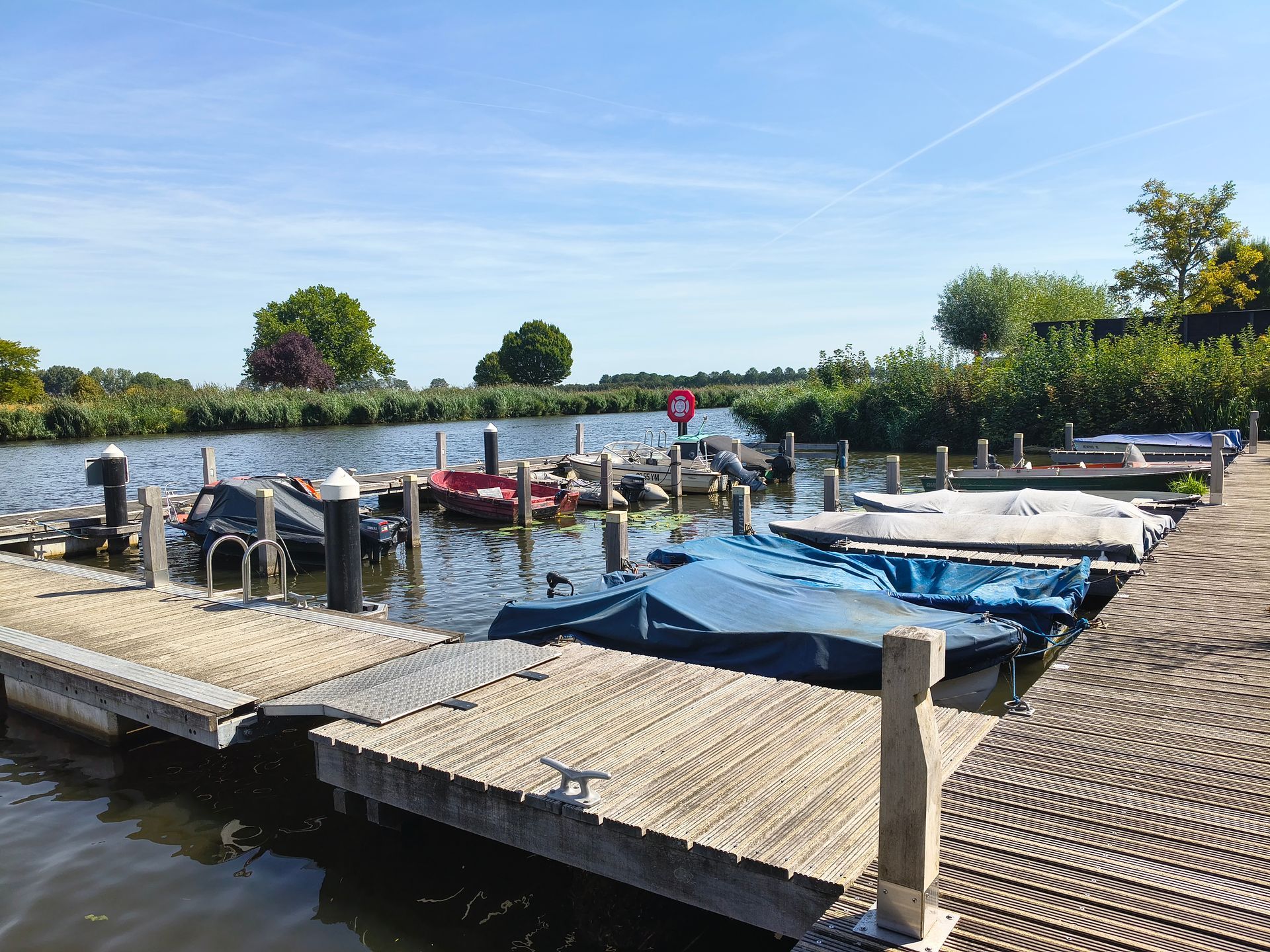 Een aanlegsteiger aan een rustig meer met aangemeerde kleine bootjes onder een heldere blauwe hemel.