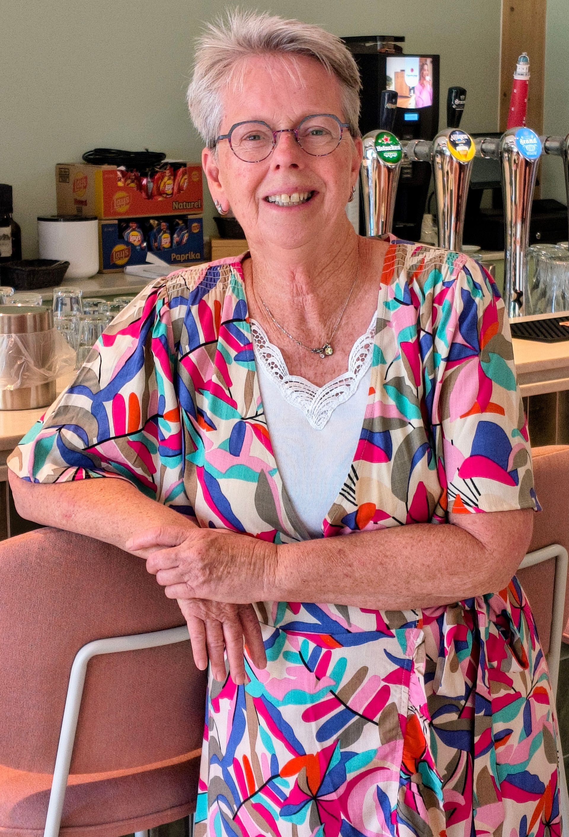 Een lachende dame in een kleurrijke blouse leunt tegen de toonbank van een café.