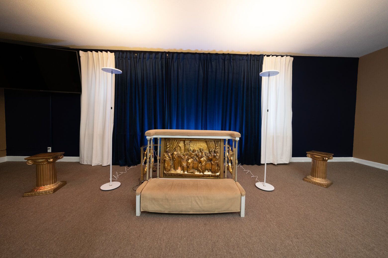 Gold altar centered on a carpeted stage, with dark curtains, white drapes, and two small side tables