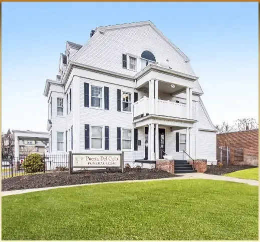 White historic house with black shutters, front porch, and a green lawn under a blue sky