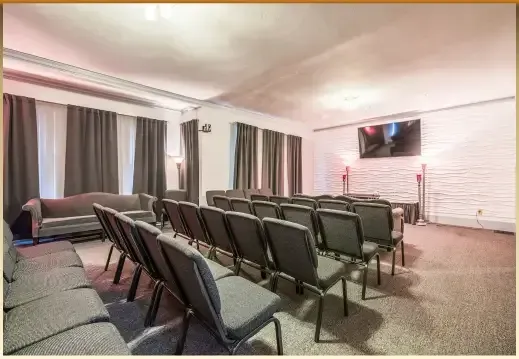 Small conference room with rows of black chairs facing a wall-mounted TV and white brick wall