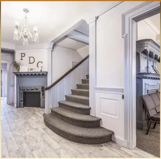 Elegant foyer with curved staircase, gray fireplace, and chandelier in a bright home interior