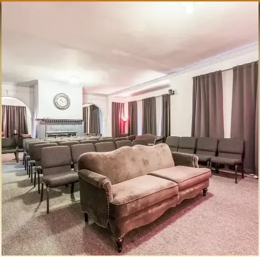 Bright waiting room with rows of brown chairs, a beige loveseat, and large curtained windows.