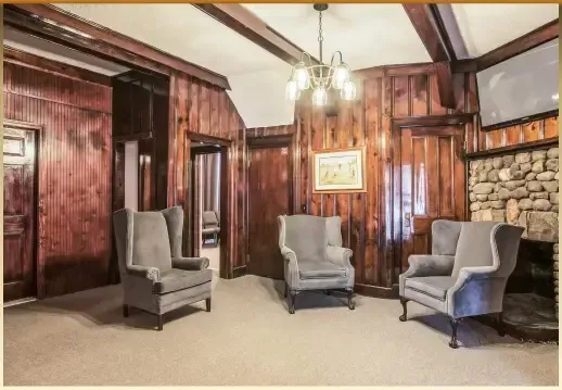 Wood-paneled room with high ceiling, gray armchairs, and a framed painting on the wall