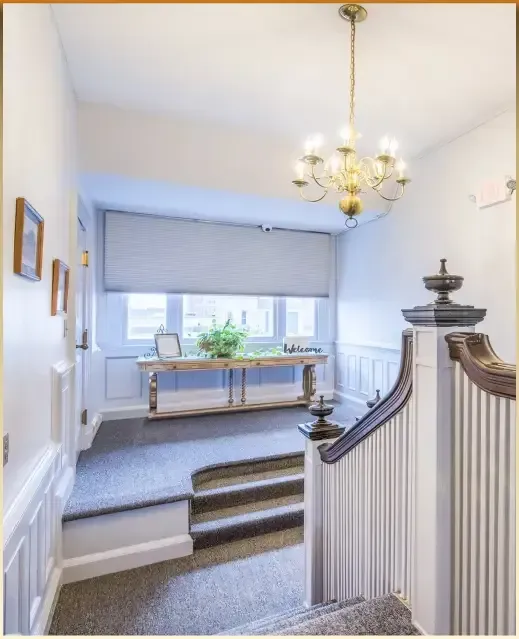 Bright hallway with carpeted steps, white walls, chandelier, and a window seat by large windows