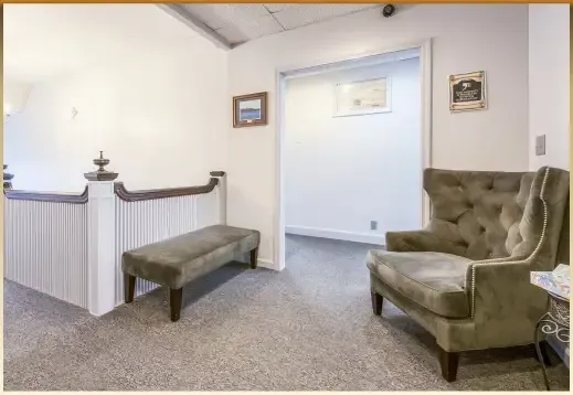 Quiet waiting room with beige carpet, green chairs, and white walls.