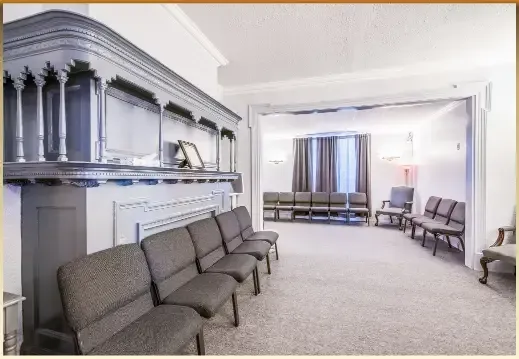 Bright funeral home room with gray chairs, white walls, and a casket display on the left
