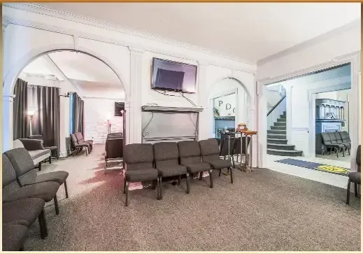 Bright lobby seating area with gray chairs, wall TV, and stairway on the right.