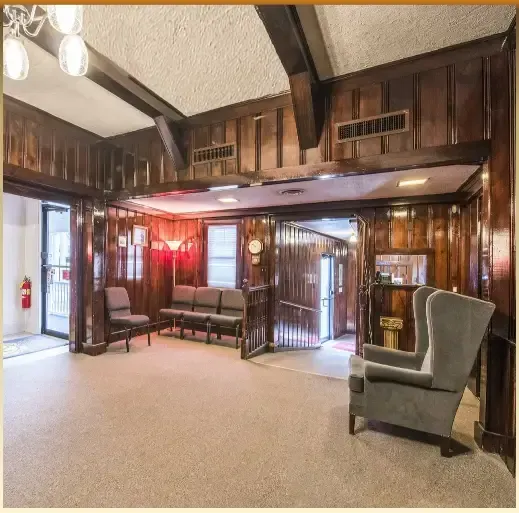 Vintage living room with wood paneling, high ceiling, armchairs, couch, and warm lighting