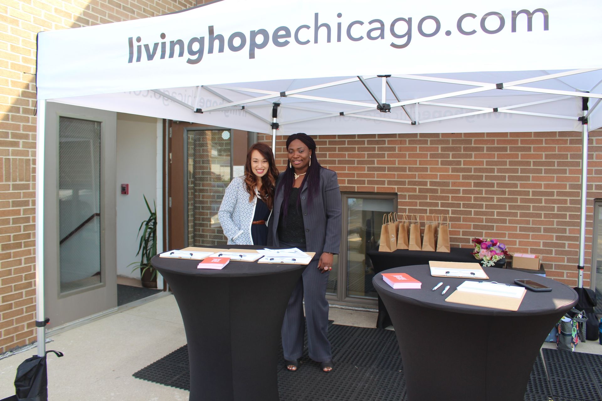 Two people stand at a covered outreach table under a tent labeled livinghopechicago.com